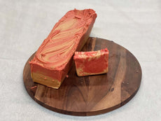 Strawberry cheesecake fudge block and piece on a wooden board displaying vibrant swirls and creamy texture.